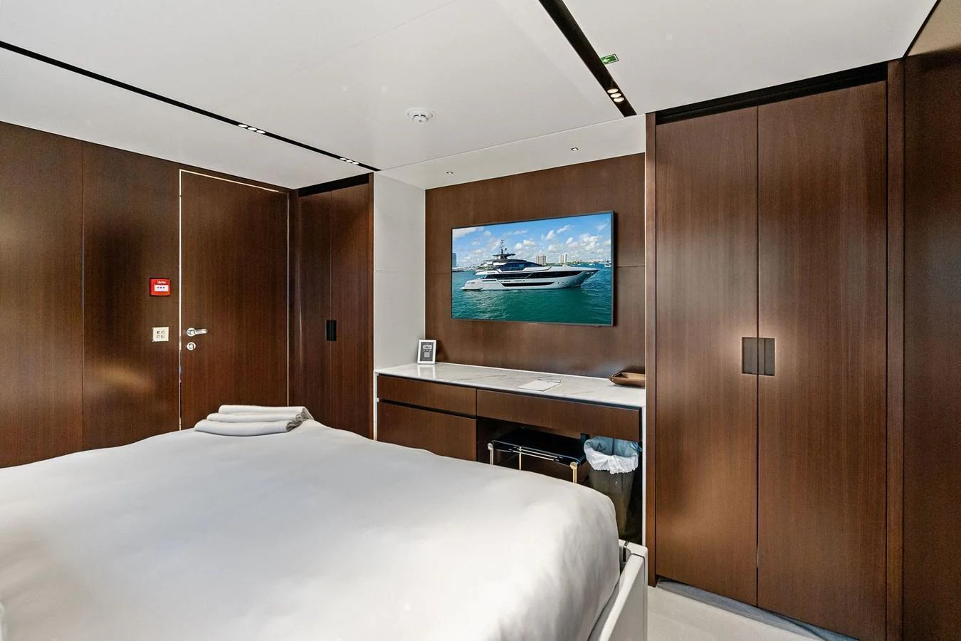 The stateroom features a large bed, sleek wooden cabinetry, and a flat-screen TV displaying a yacht image. aboard TENACIOUS Yacht for Sale