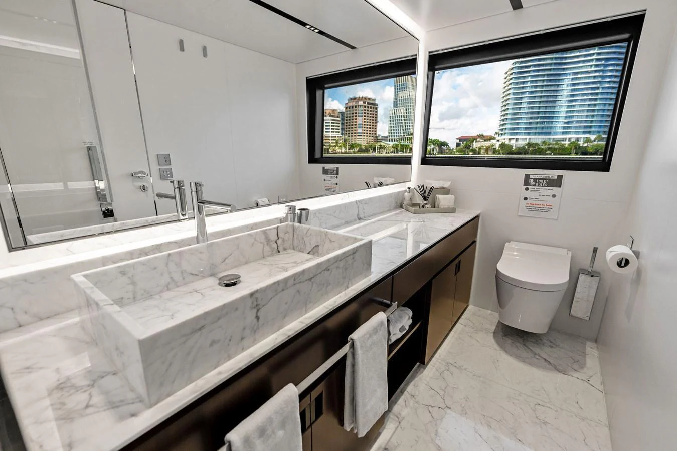 The yacht's bathroom features a sleek, modern design with a marble countertop and large windows offering a view of the cityscape. aboard TENACIOUS Yacht for Sale