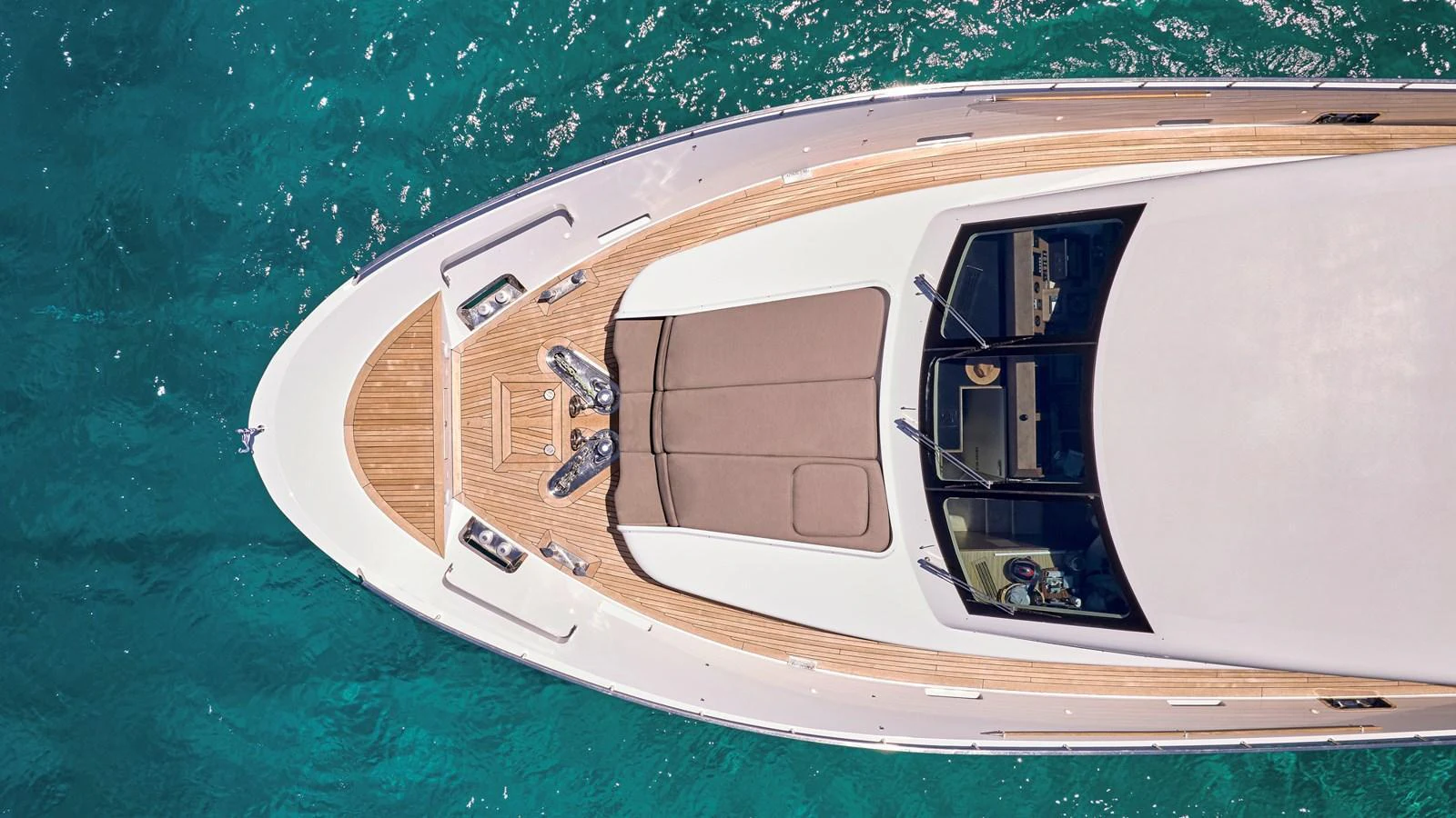 The foredeck of the yacht showcases a sleek design with a sunpad and teak decking, set against the backdrop of clear blue waters. aboard MILGAUSS Yacht for Sale
