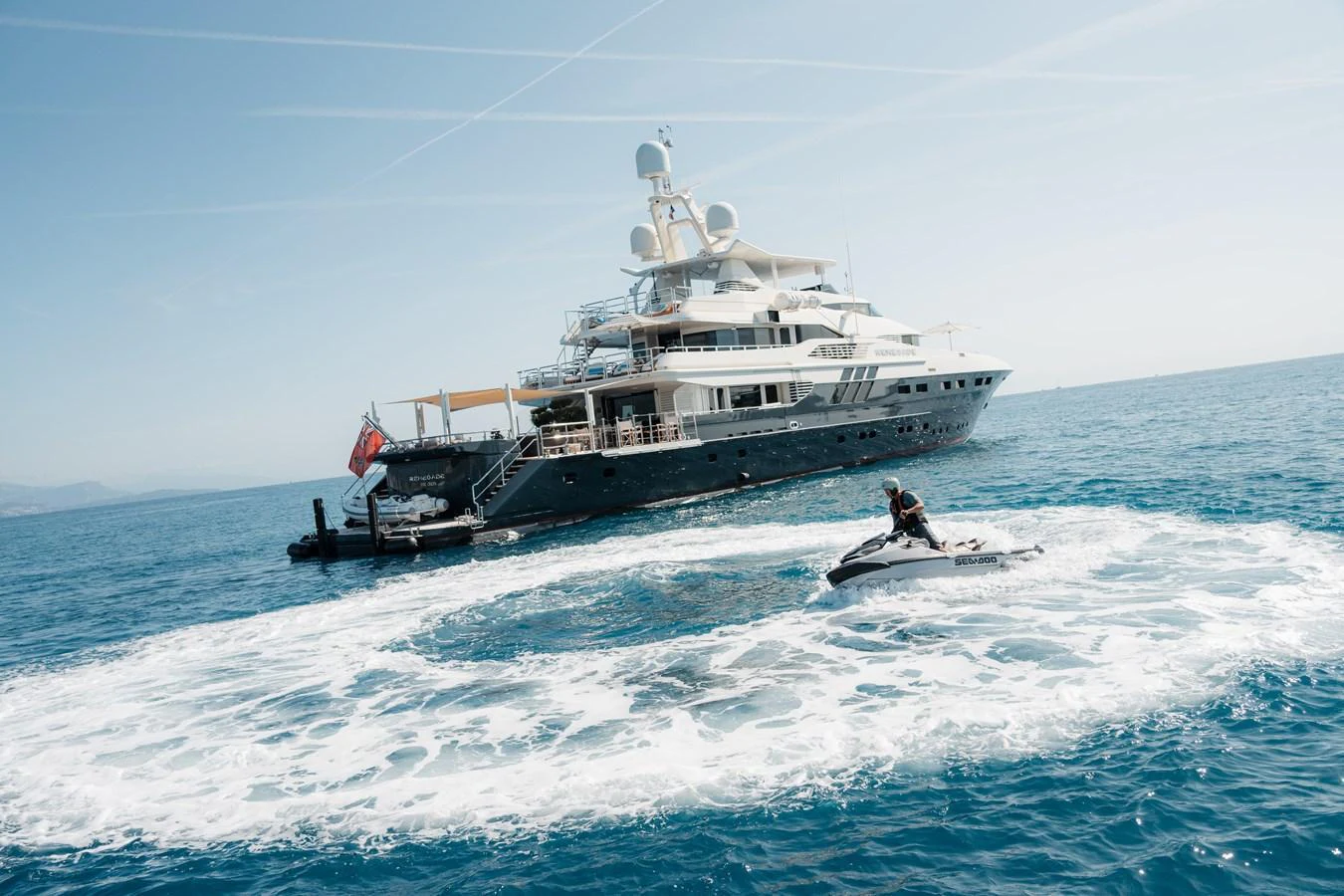 A luxurious yacht anchored on the open sea with a person riding a jet ski nearby. aboard RENEGADE Yacht for Sale