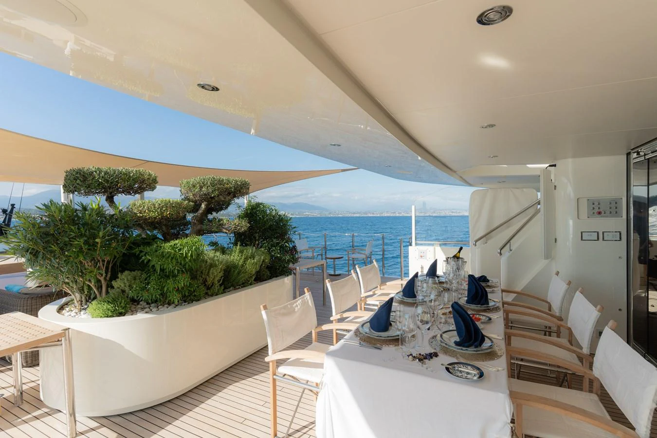 The aft deck features an elegant dining area with a beautifully set table and lush greenery, offering a serene ocean view. aboard RENEGADE Yacht for Sale