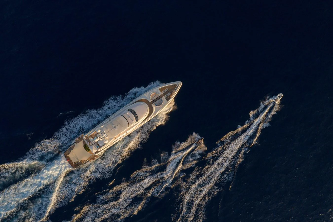 An aerial view of a sleek yacht cruising through the water with a tender following closely behind. aboard RENEGADE Yacht for Sale