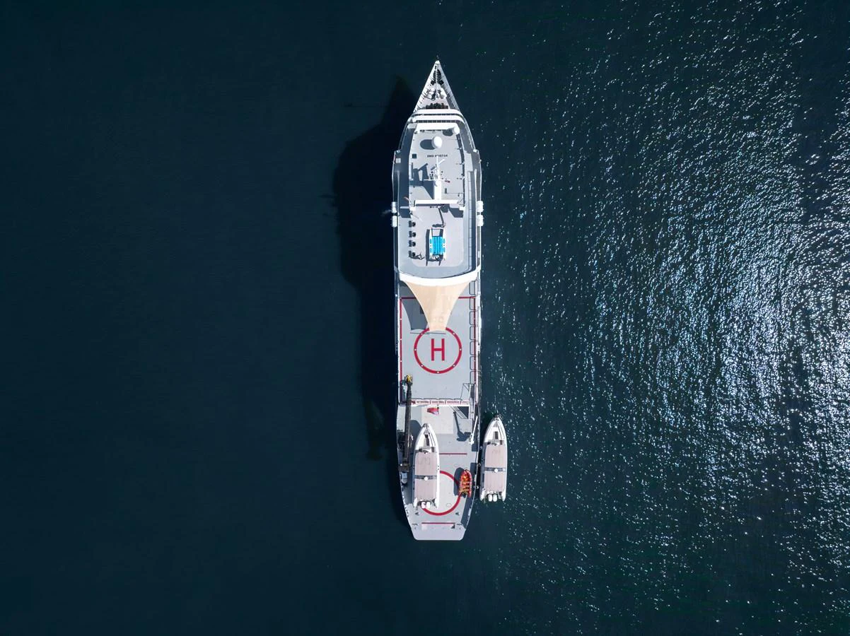 Aerial view of a luxurious yacht with a helipad and tenders on calm waters. aboard GLOBAL Yacht for Sale