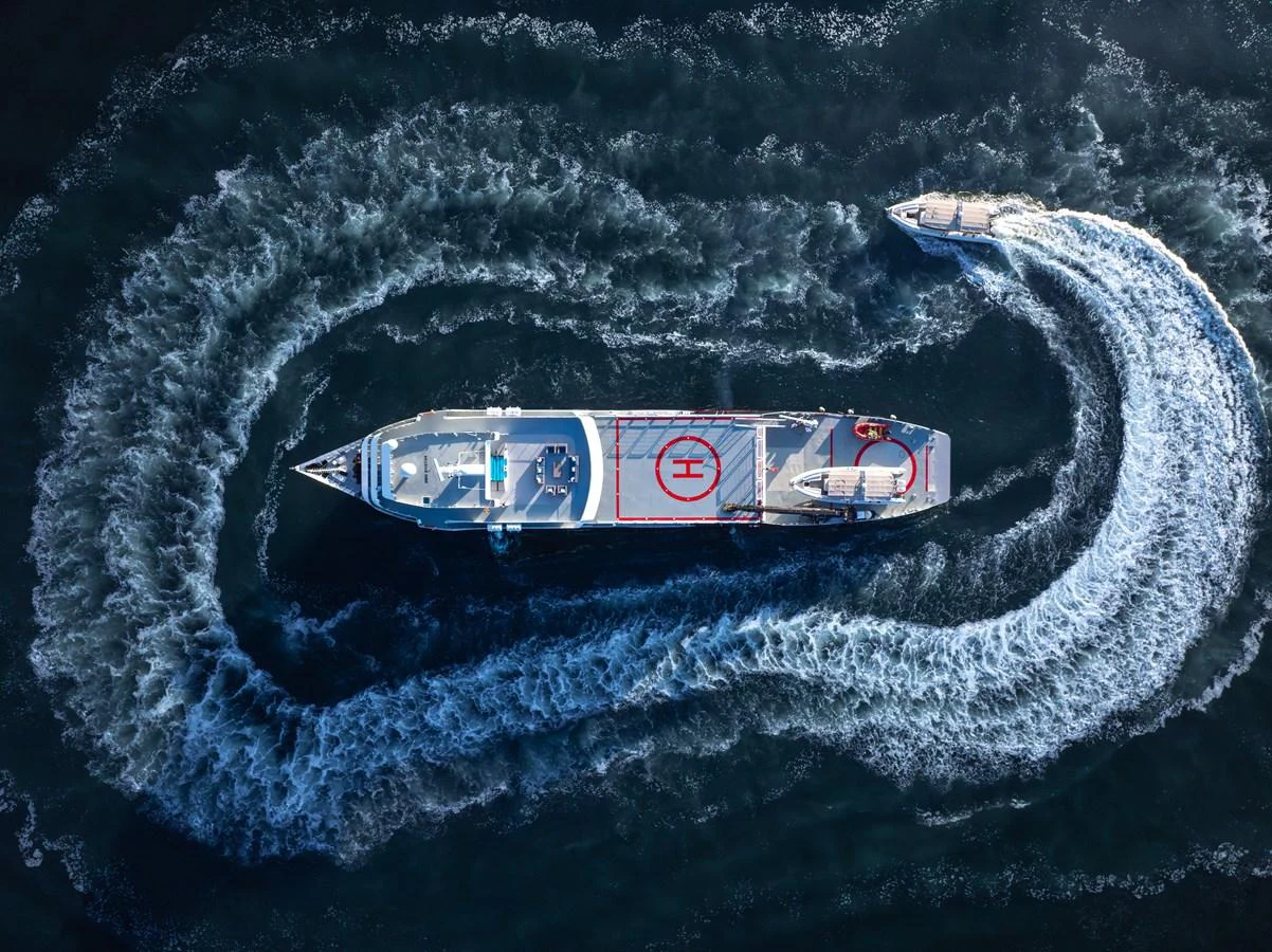 Aerial view of a yacht with a helipad, creating a dramatic wake pattern in the water. aboard GLOBAL Yacht for Sale