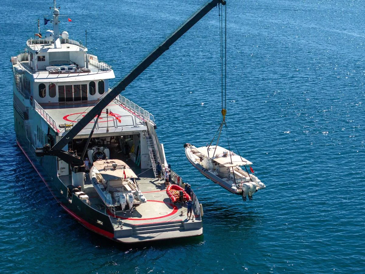 The yacht's tender is being lowered into the water by a crane, showcasing the vessel's practical capabilities. aboard GLOBAL Yacht for Sale