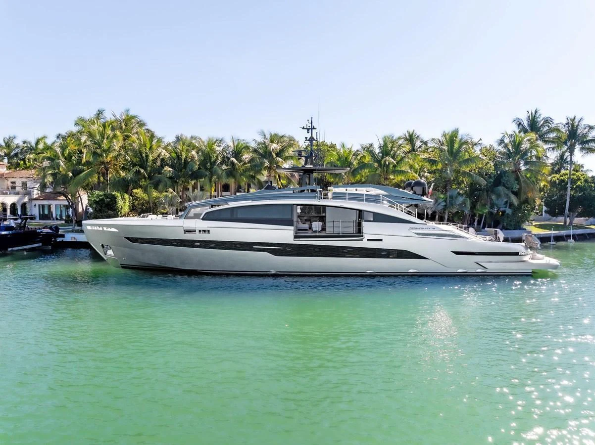 A sleek, modern yacht glides gracefully on tranquil turquoise waters, framed by lush palm trees in the background. aboard CAFFEINE Yacht for Sale
