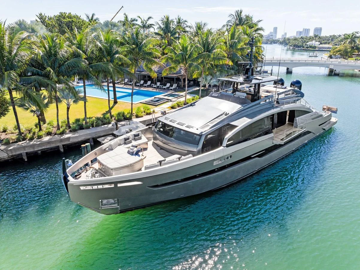 A sleek and modern yacht is docked in a serene marina surrounded by lush palm trees and clear waters. aboard CAFFEINE Yacht for Sale