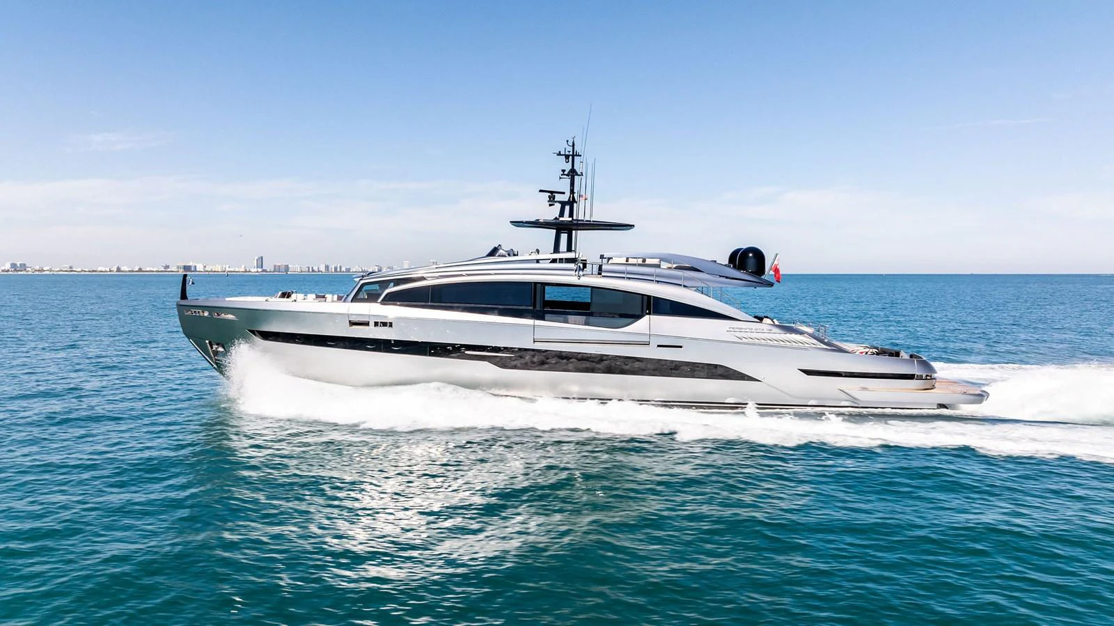 A sleek and modern yacht glides swiftly across the open sea under a clear blue sky. aboard CAFFEINE Yacht for Sale