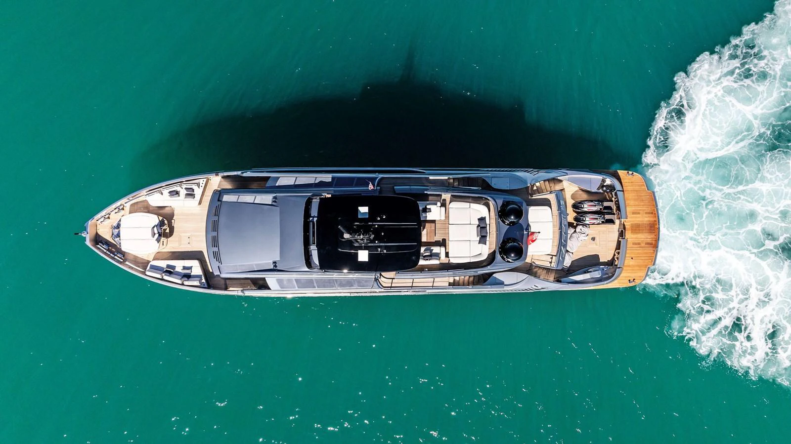 A sleek yacht cruises through clear turquoise waters, showcasing its elegant design from an aerial perspective. aboard CAFFEINE Yacht for Sale