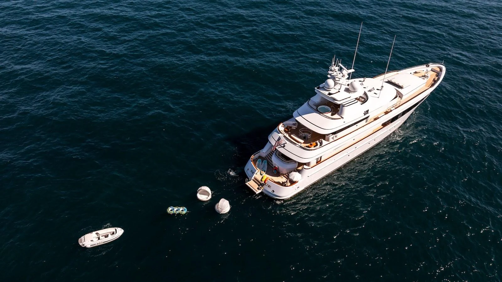 A luxurious yacht is anchored in calm waters, accompanied by a tender and water toys. aboard MYSTIQUE Yacht for Sale