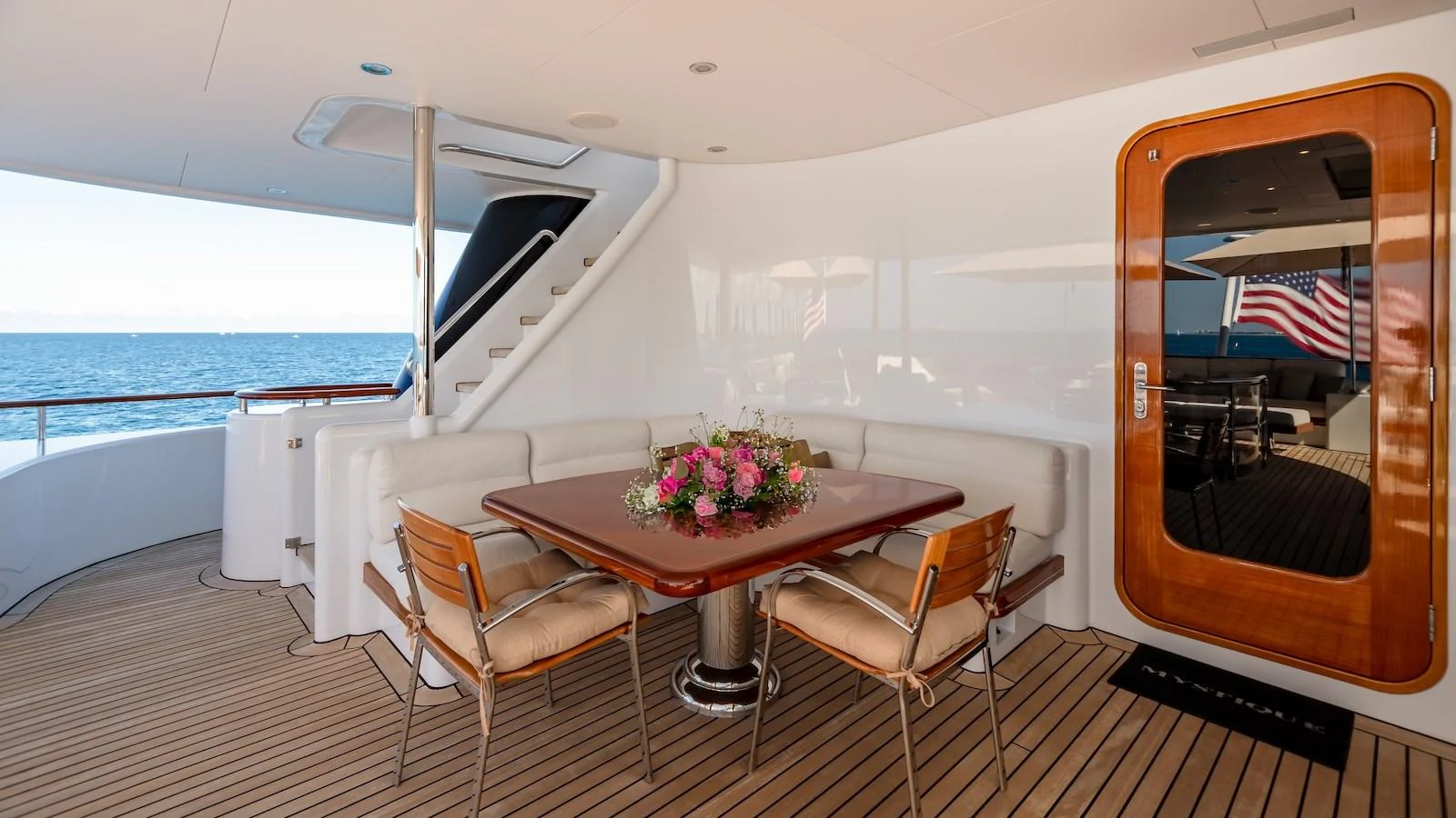 The aft deck features a stylish dining area with a wooden table and comfortable seating, perfect for enjoying meals with a view of the sea. aboard MYSTIQUE Yacht for Sale