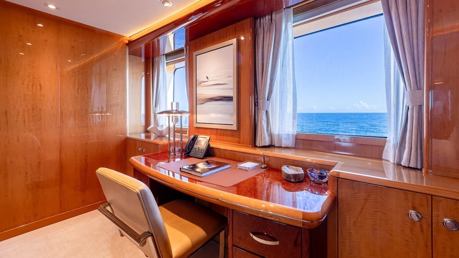 The yacht's office features a sleek wooden desk with a stunning ocean view through large windows. aboard MYSTIQUE Yacht for Sale