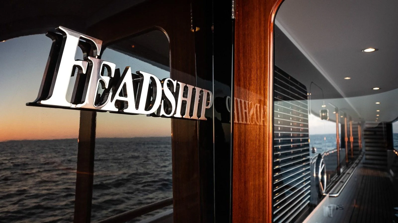 A close-up view of the yacht's exterior showcasing the Feadship logo and sleek wooden finish at sunset. aboard MYSTIQUE Yacht for Sale