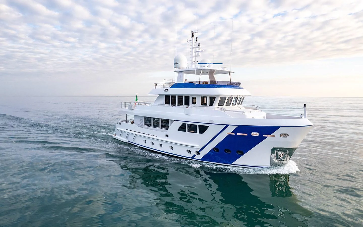 A sleek yacht glides across calm waters under a partly cloudy sky. aboard EMPIRE Yacht for Sale