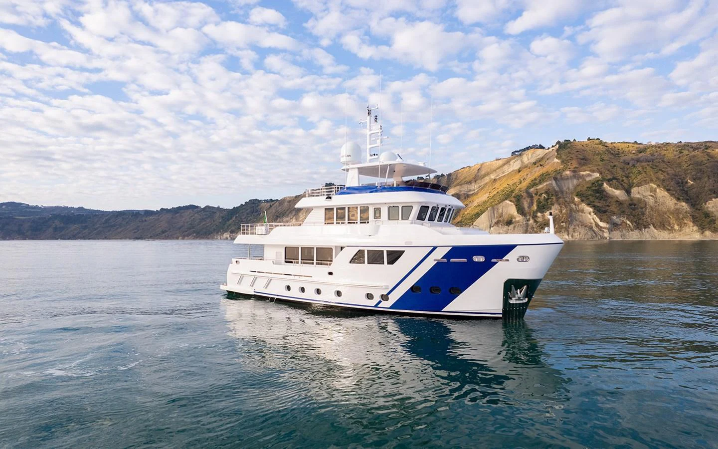 A stunning yacht glides gracefully on calm waters with a scenic coastal backdrop. aboard EMPIRE Yacht for Sale