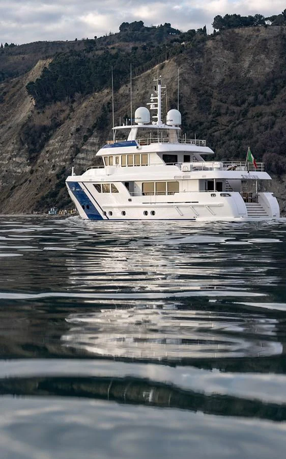A luxurious yacht cruises along a serene coastline, reflecting beautifully on the calm water. aboard EMPIRE Yacht for Sale