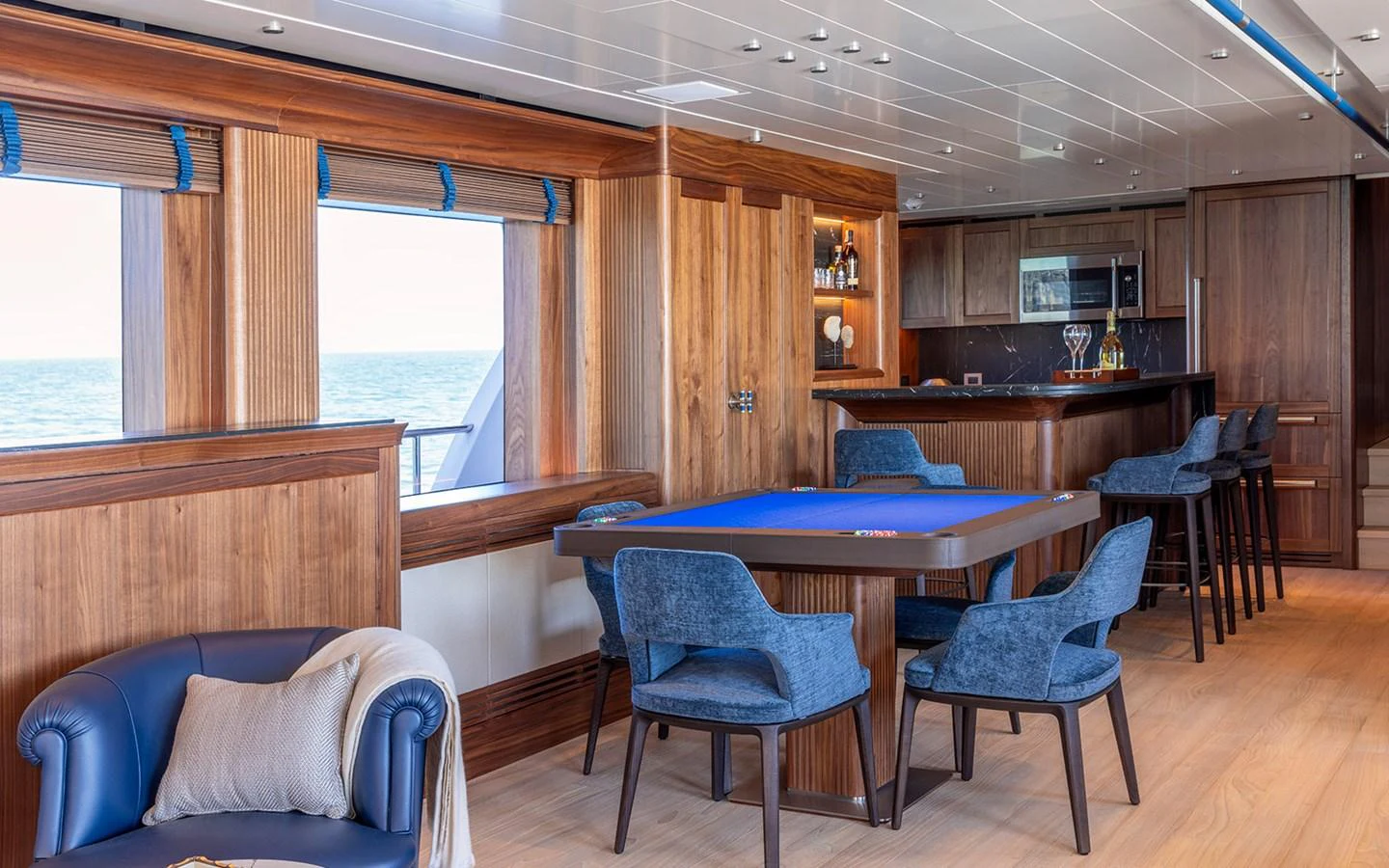 The yacht's lounge features a stylish blend of wood and blue tones, with a card table and bar area for entertainment. aboard EMPIRE Yacht for Sale