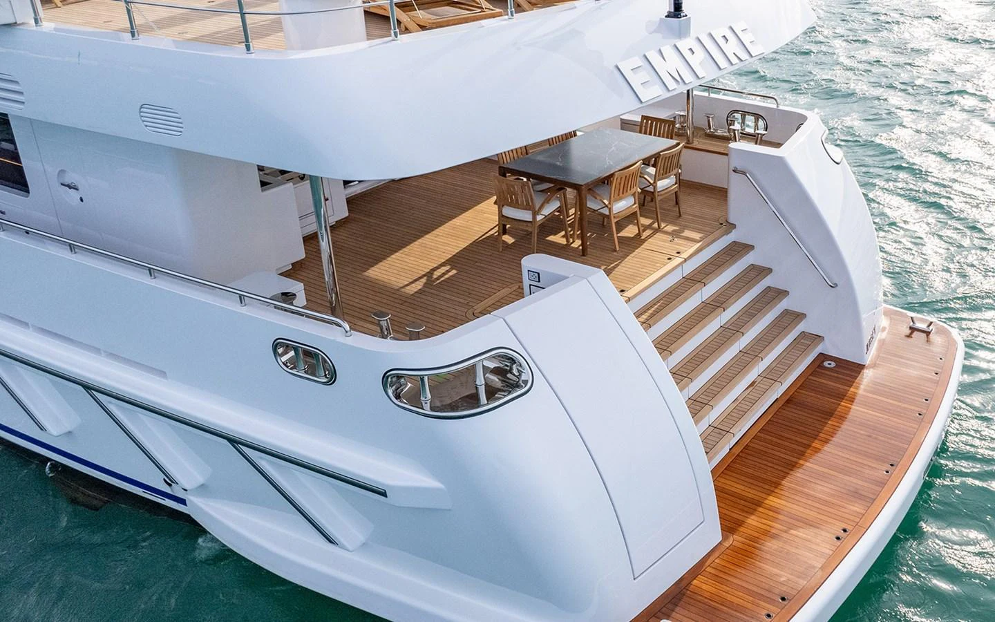 The yacht's aft deck features a spacious seating area with a wooden table and chairs, perfect for alfresco dining. aboard EMPIRE Yacht for Sale