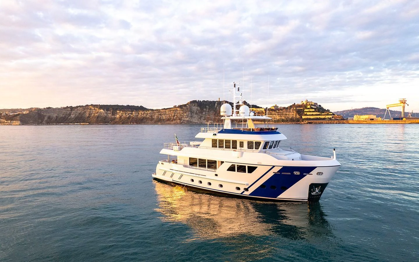 A luxurious yacht cruises peacefully on calm waters with a scenic coastal backdrop. aboard EMPIRE Yacht for Sale