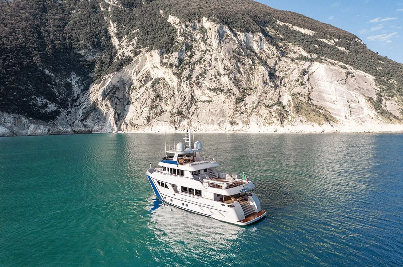A luxurious yacht cruises along a stunning coastal landscape with clear turquoise waters and rugged cliffs. aboard EMPIRE Yacht for Sale