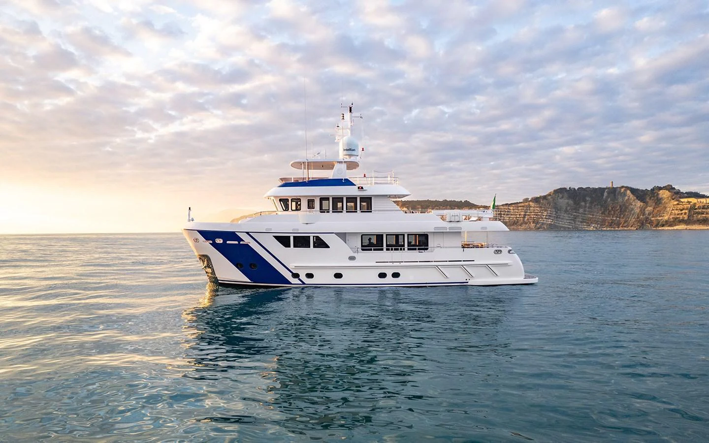 A stunning yacht glides gracefully on calm waters against a picturesque coastal backdrop. aboard EMPIRE Yacht for Sale