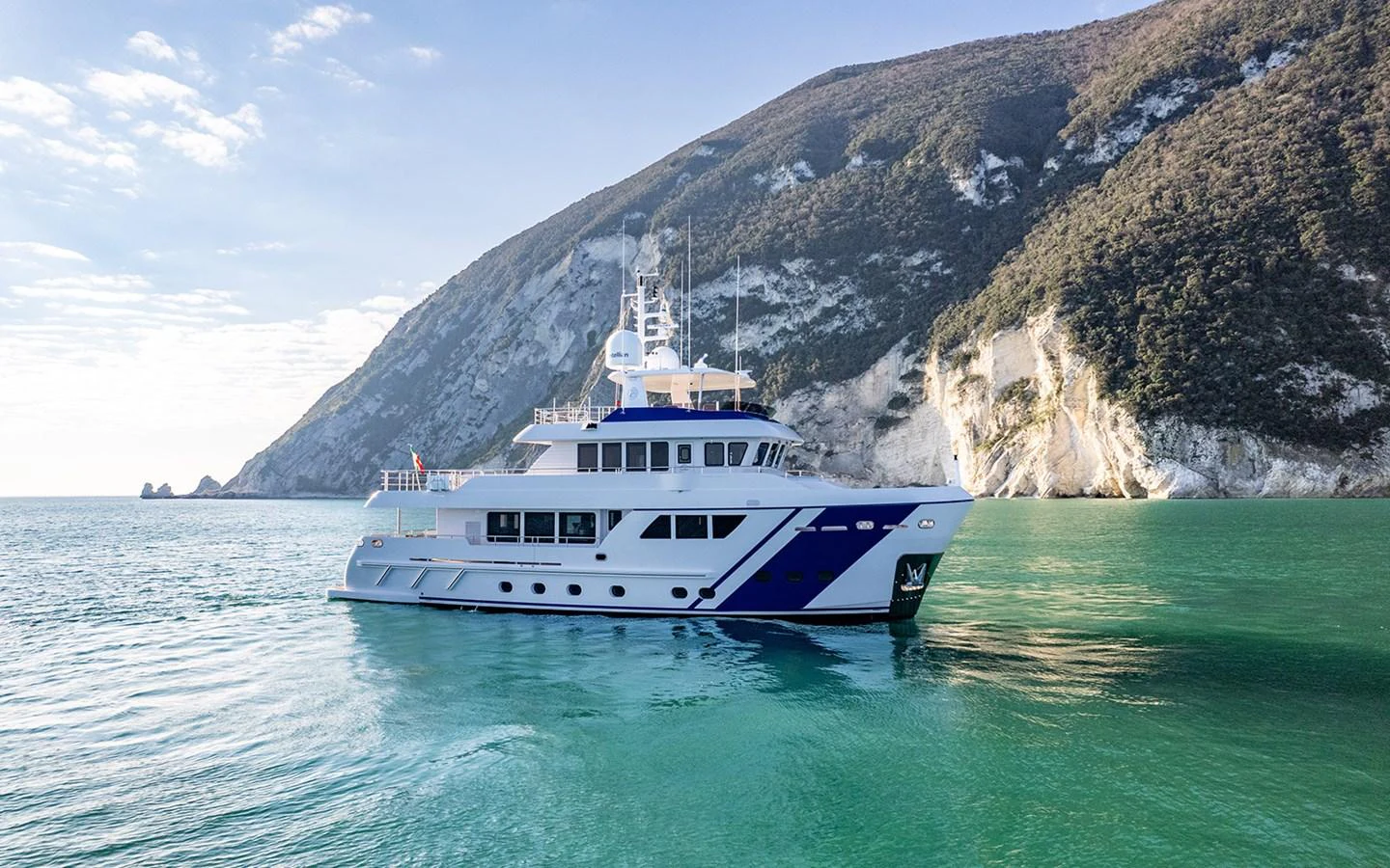 A luxurious yacht cruises through serene turquoise waters against a backdrop of majestic cliffs. aboard EMPIRE Yacht for Sale