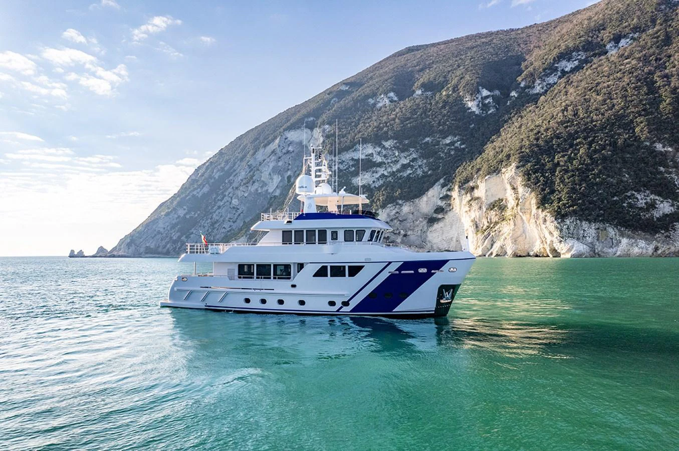 A stunning yacht cruises serenely in a picturesque coastal setting with clear blue waters and scenic cliffs. aboard EMPIRE Yacht for Sale