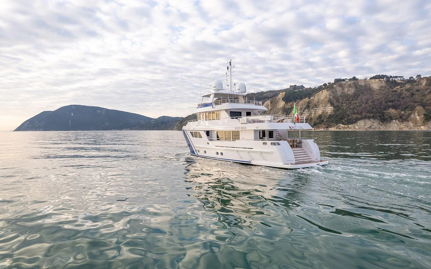 A luxurious yacht cruises through calm waters with scenic hills in the background. aboard EMPIRE Yacht for Sale