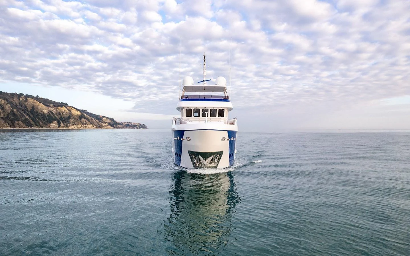 A majestic yacht cruises forward on calm waters under a partly cloudy sky. aboard EMPIRE Yacht for Sale