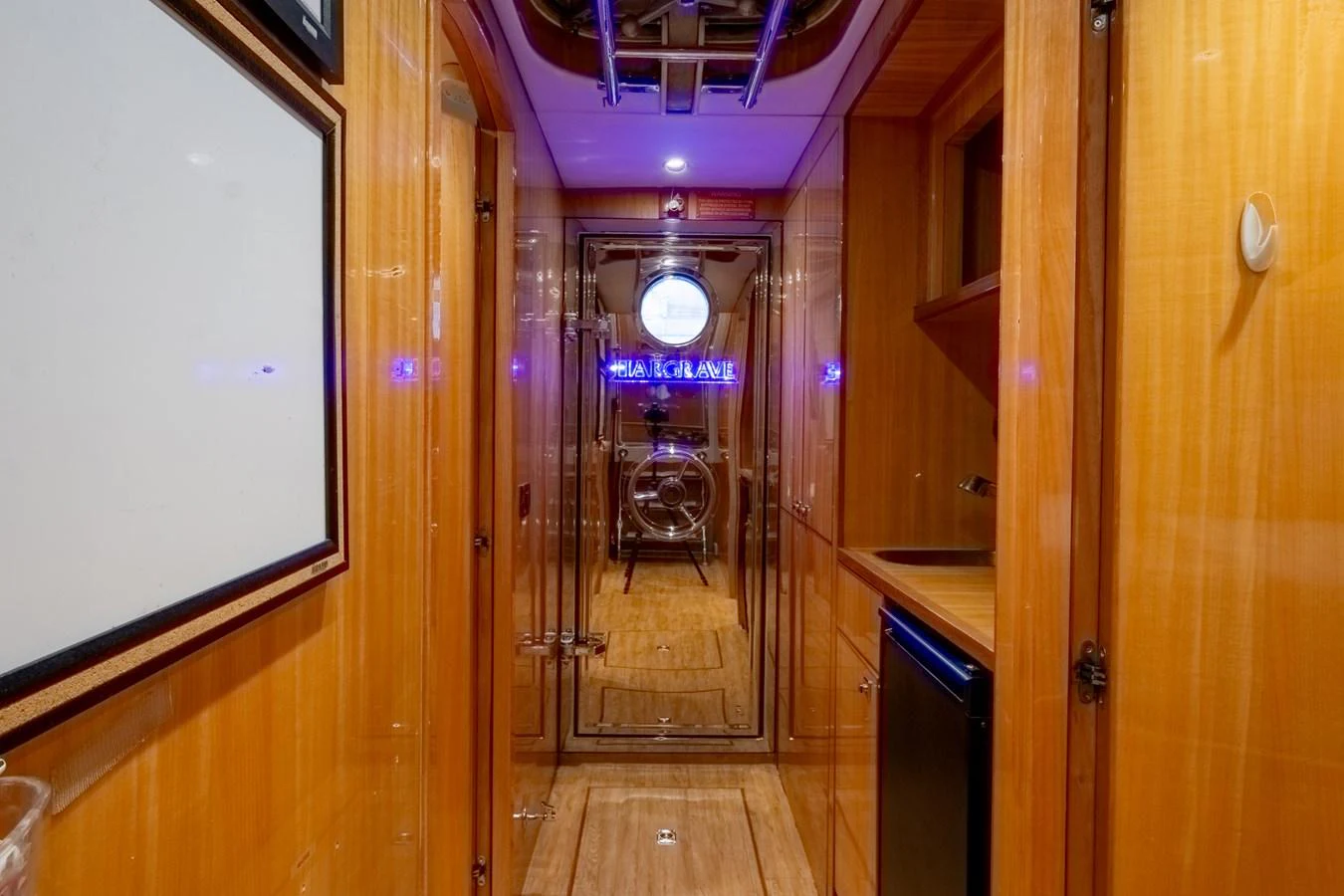 A polished hallway with wooden paneling and modern lighting leads to a door with a porthole window. aboard LUCKY PENNY Yacht for Sale