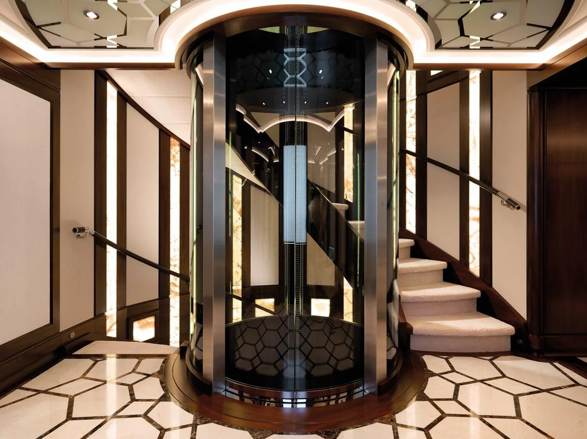 The elegant interior features a luxurious staircase with a modern glass elevator. aboard JUST J'S Yacht for Sale