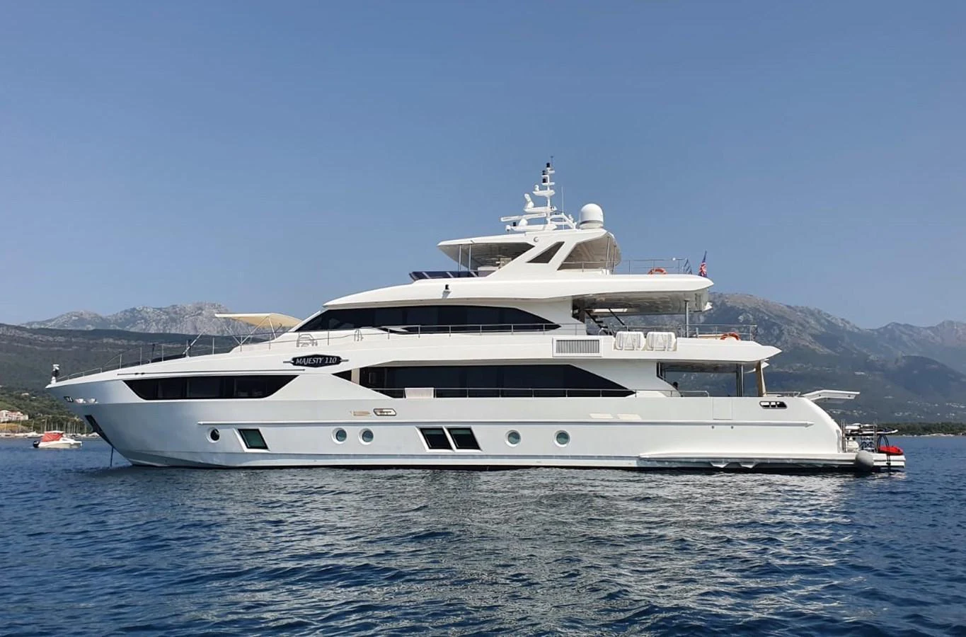 A sleek and modern yacht glides gracefully on calm waters with a mountainous backdrop. aboard AMORE Yacht for Sale