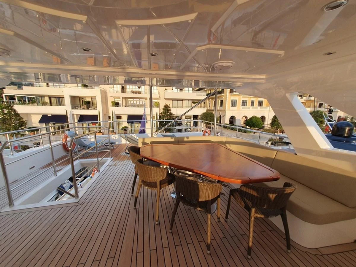 The aft deck features a spacious dining area with a polished wooden table and comfortable seating, perfect for alfresco dining. aboard AMORE Yacht for Sale