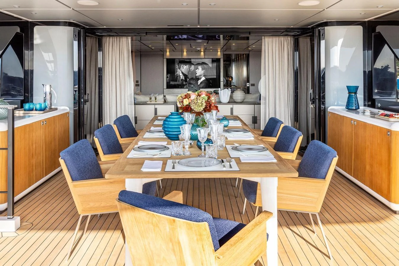 The yacht's dining area features a stylish setup with a wooden table and comfortable blue-cushioned chairs, perfect for an elegant meal at sea. aboard MIOTU Yacht for Sale