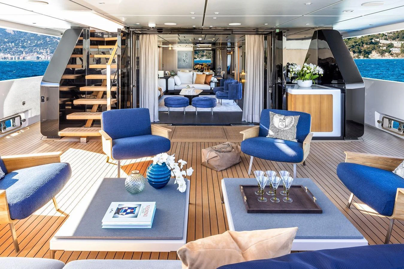 The aft deck features a luxurious seating area with blue cushions and a view into the stylish interior. aboard MIOTU Yacht for Sale