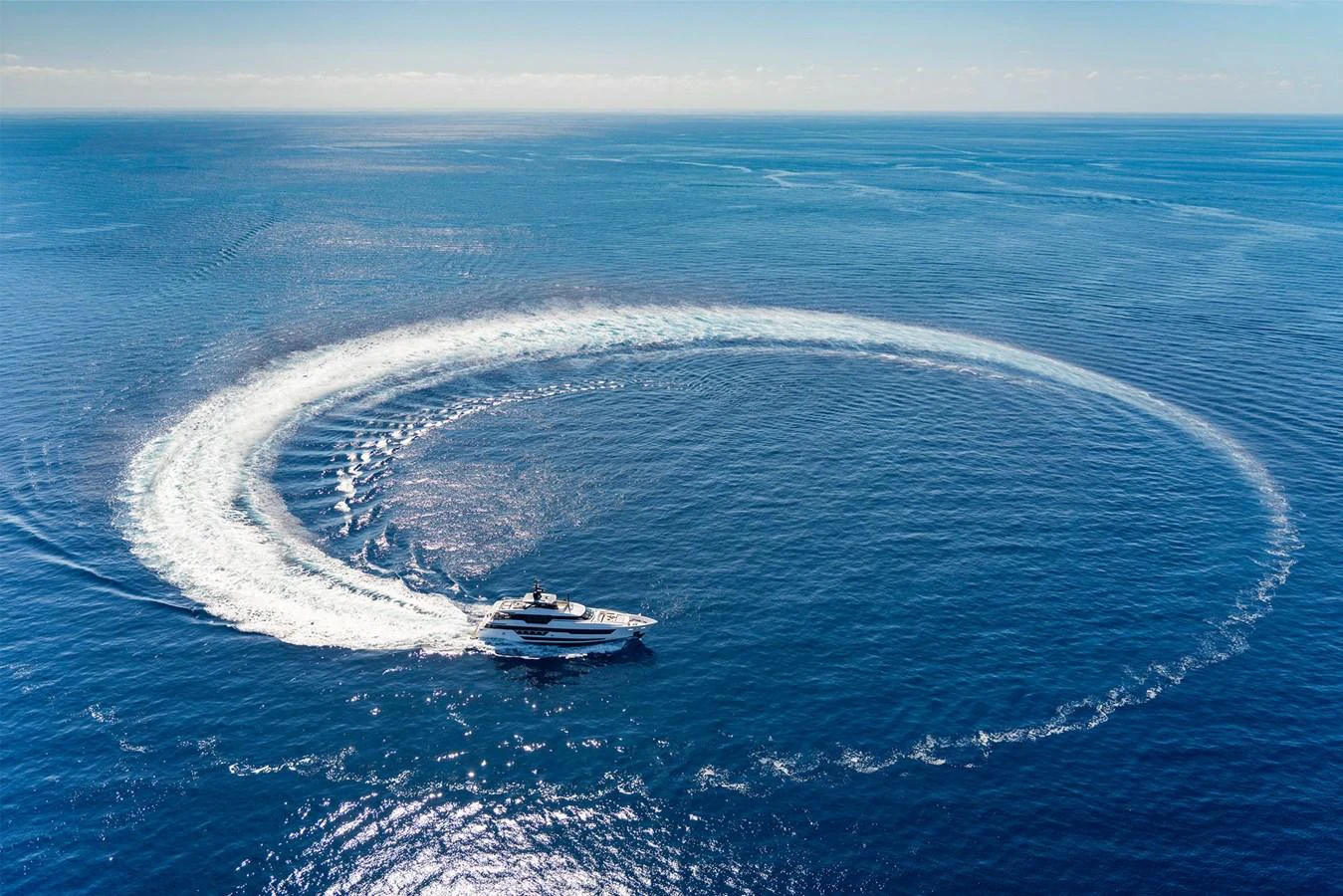 A sleek yacht gracefully maneuvers in a wide circle on the open sea, leaving a striking wake pattern behind. aboard MIOTU Yacht for Sale