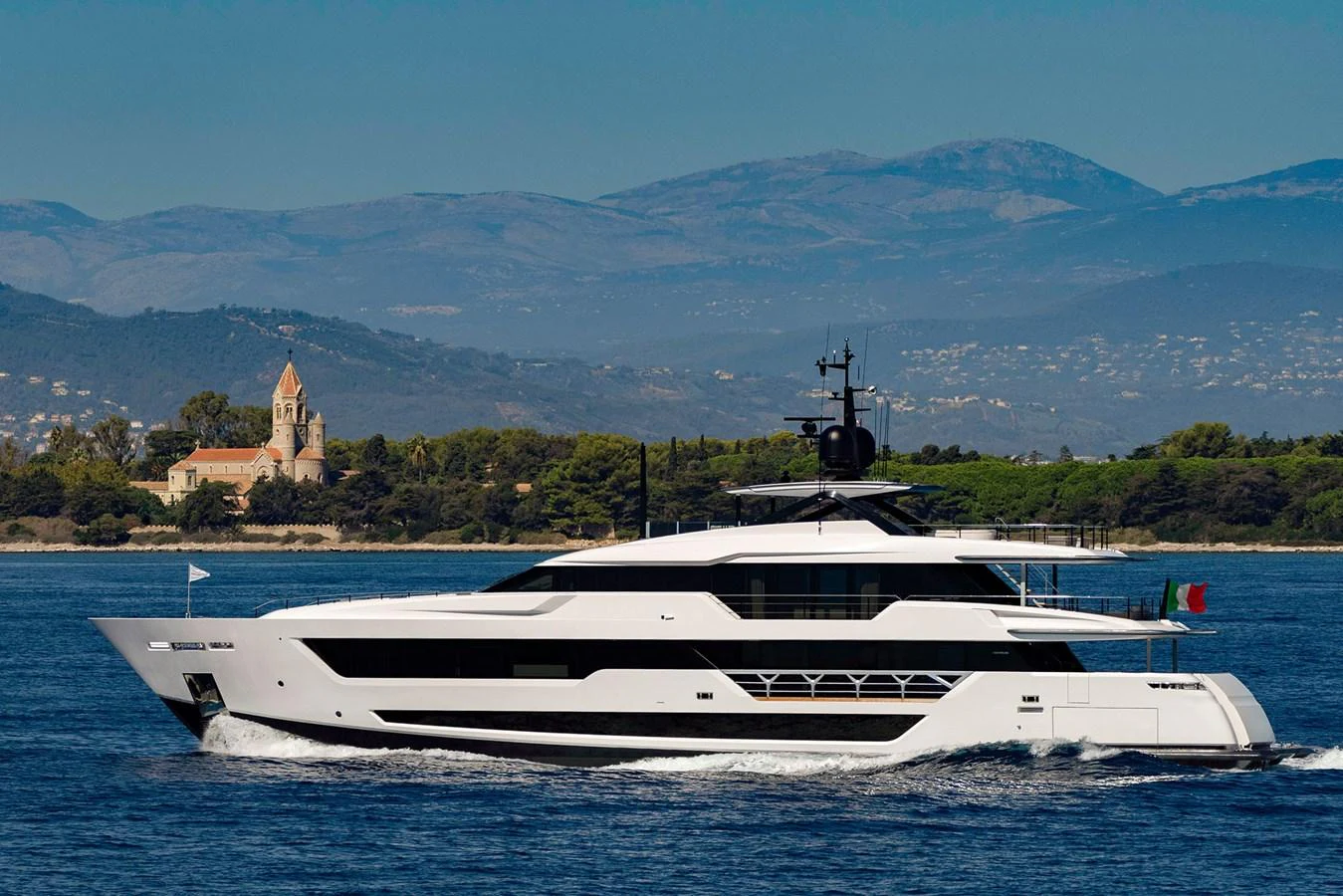 A sleek and modern yacht cruises along the coast with scenic mountains in the background. aboard MIOTU Yacht for Sale
