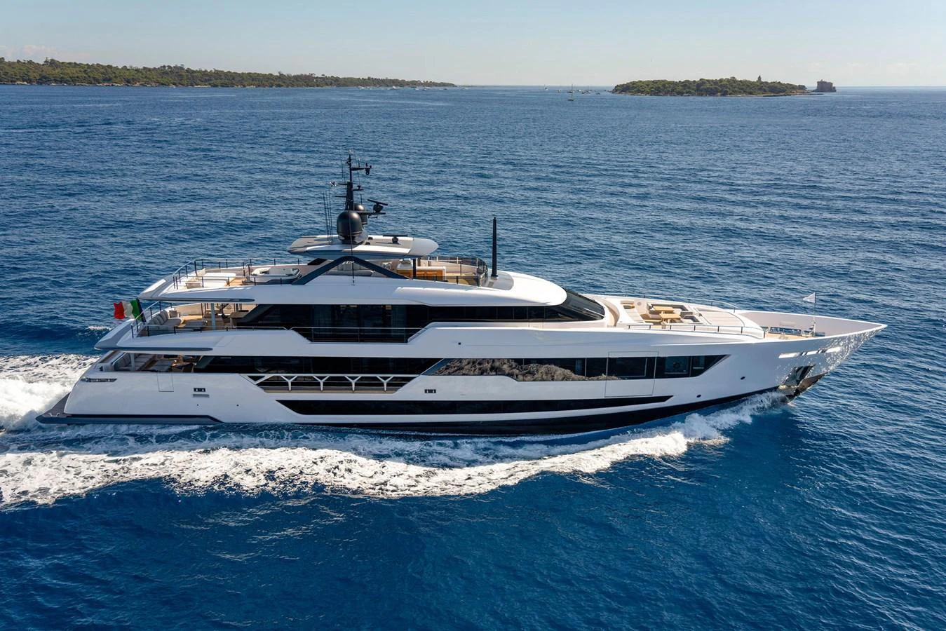 A sleek and modern yacht cruises through clear blue waters with an island in the background. aboard MIOTU Yacht for Sale
