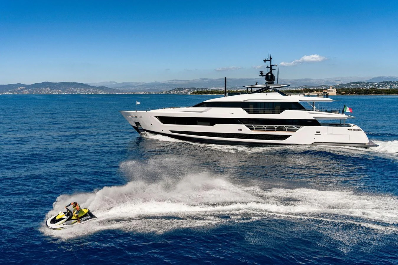 A sleek and modern yacht cruises on the open water with a jet ski speeding alongside. aboard MIOTU Yacht for Sale