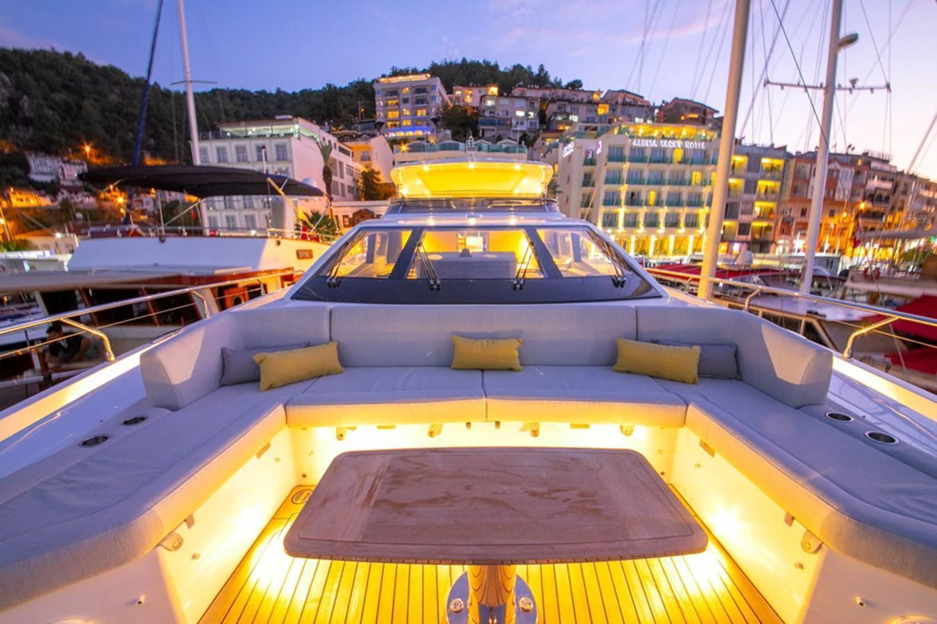 The aft deck of the yacht is beautifully illuminated, offering a cozy seating area with a scenic backdrop of a marina at dusk. aboard NIRVANA BY THE SEA Yacht for Sale