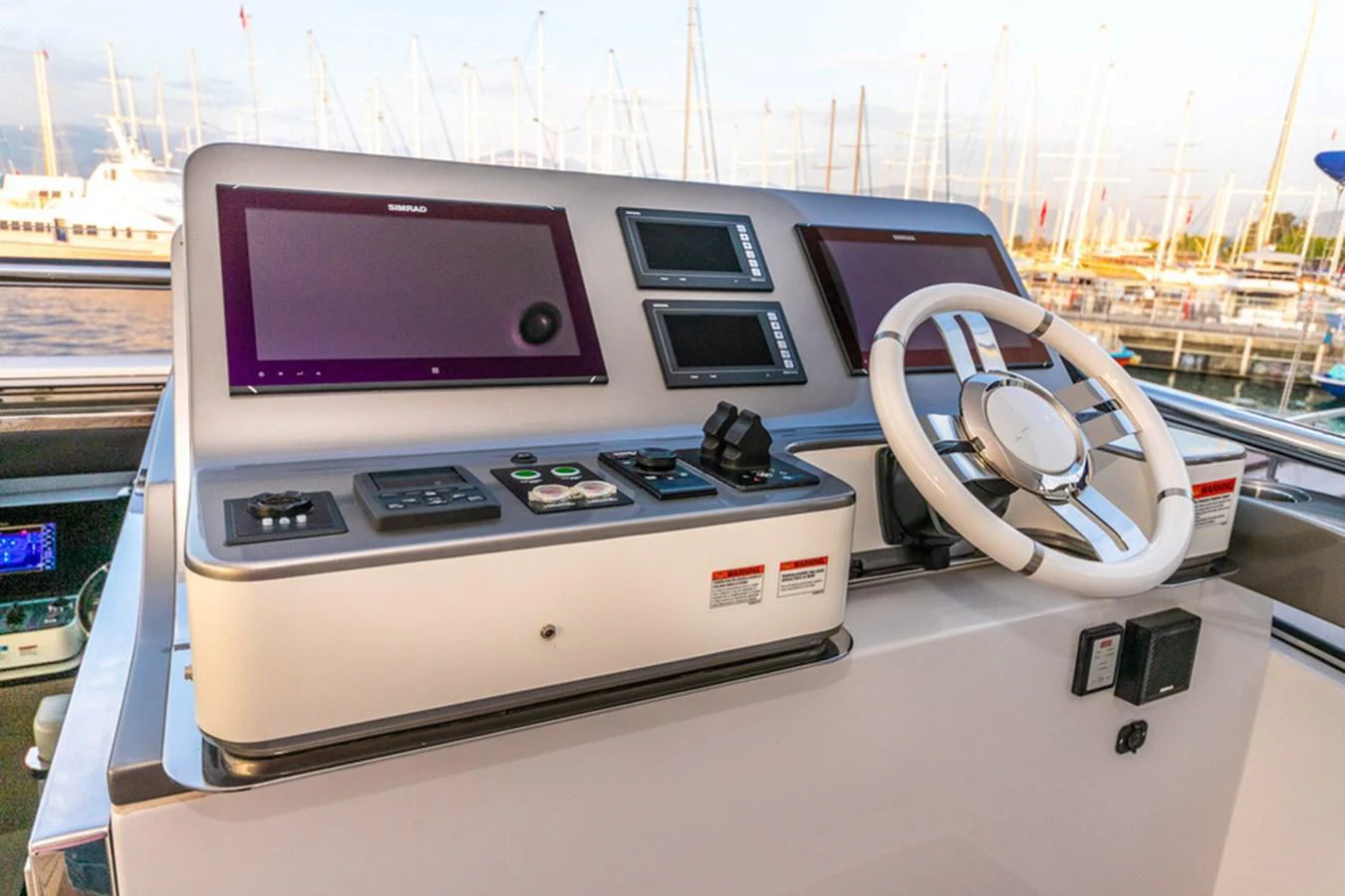 The helm station features modern navigation equipment and a sleek steering wheel, offering a commanding view of the marina. aboard NIRVANA BY THE SEA Yacht for Sale