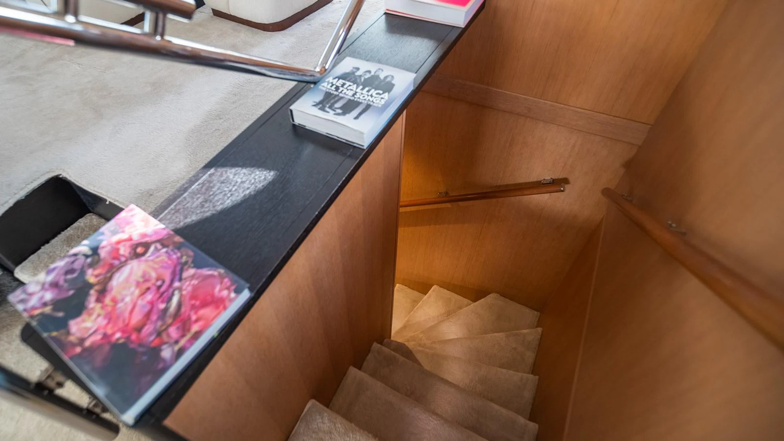 A cozy interior staircase with wooden paneling and a black handrail, leading to the lower deck. aboard TAYGET Yacht for Sale