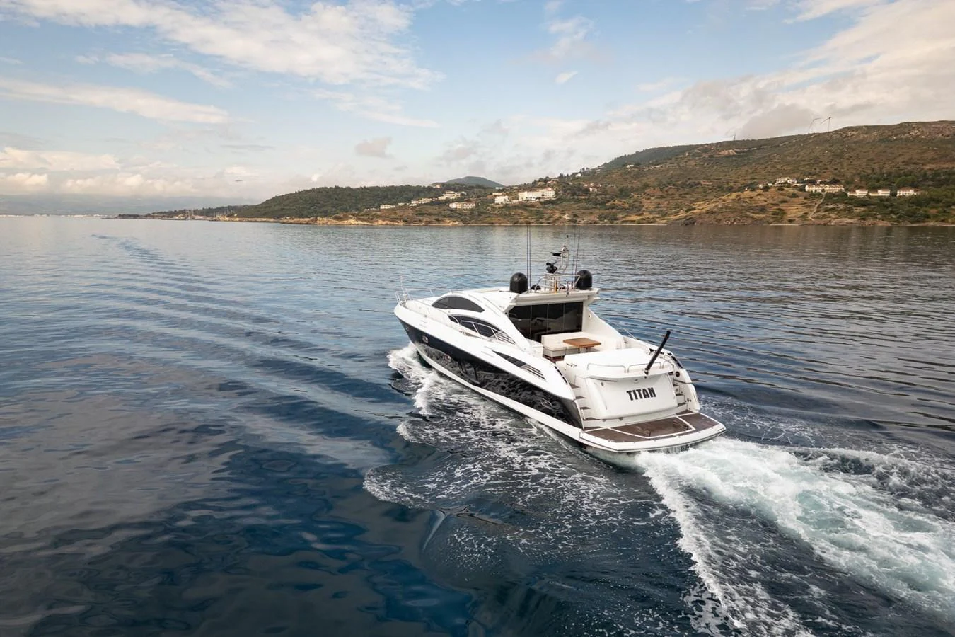 A sleek yacht cruises through calm waters with a scenic coastline in the background. aboard M/Y TITAN Yacht for Sale