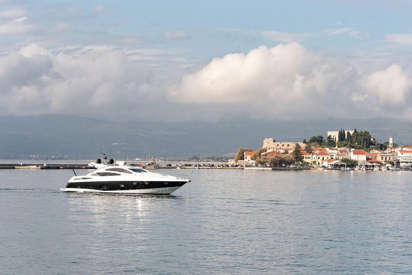 A sleek yacht cruises gracefully on calm waters with a picturesque coastal town in the background. aboard M/Y TITAN Yacht for Sale