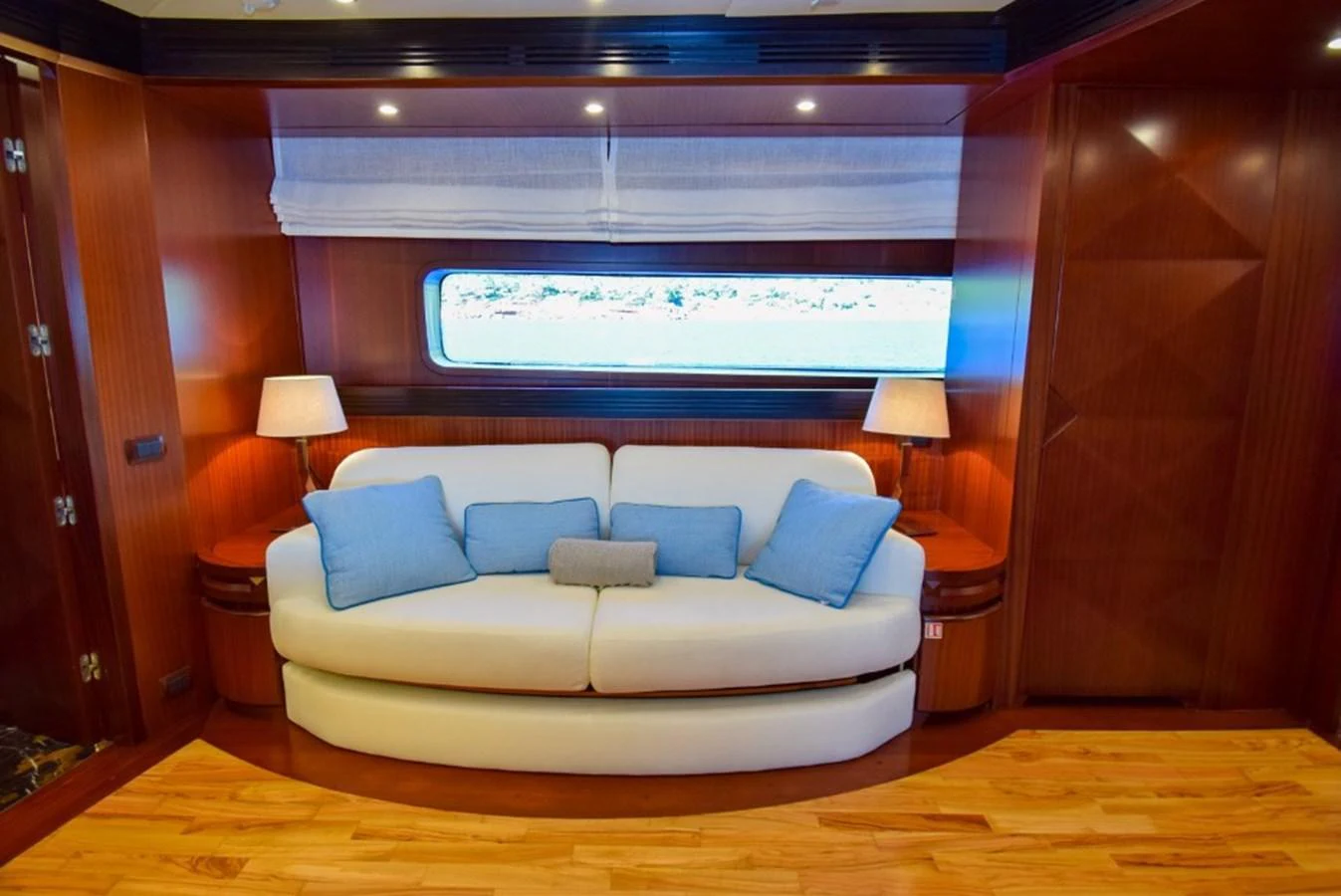 A cozy salon area with a plush white sofa and blue accent pillows, complemented by warm wooden paneling and soft lighting. aboard HOLIDAY Yacht for Sale