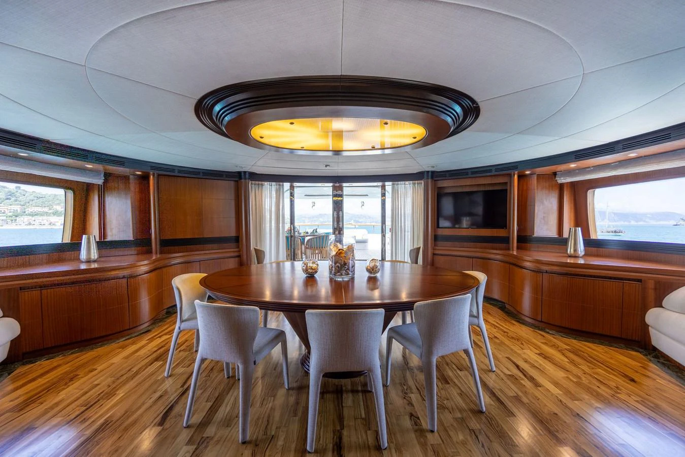 The yacht's dining area features a large round table surrounded by elegant chairs, with panoramic windows offering stunning views. aboard HOLIDAY Yacht for Sale