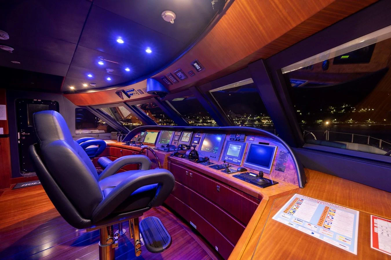 The helm station features advanced navigation equipment and luxurious wood finishes, illuminated by ambient blue lighting. aboard HOLIDAY Yacht for Sale