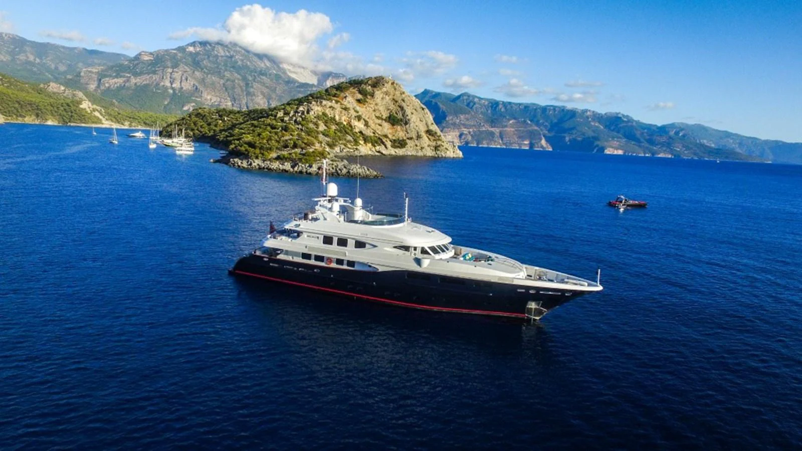 A luxurious yacht is anchored in a serene bay with stunning mountainous scenery in the background. aboard HOLIDAY Yacht for Sale