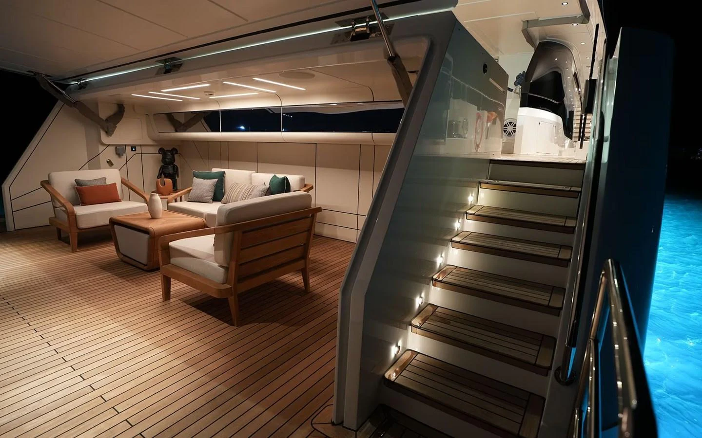 The aft deck features elegant seating and a staircase leading to the upper deck, illuminated by ambient lighting. aboard GEULUNEL Yacht for Sale