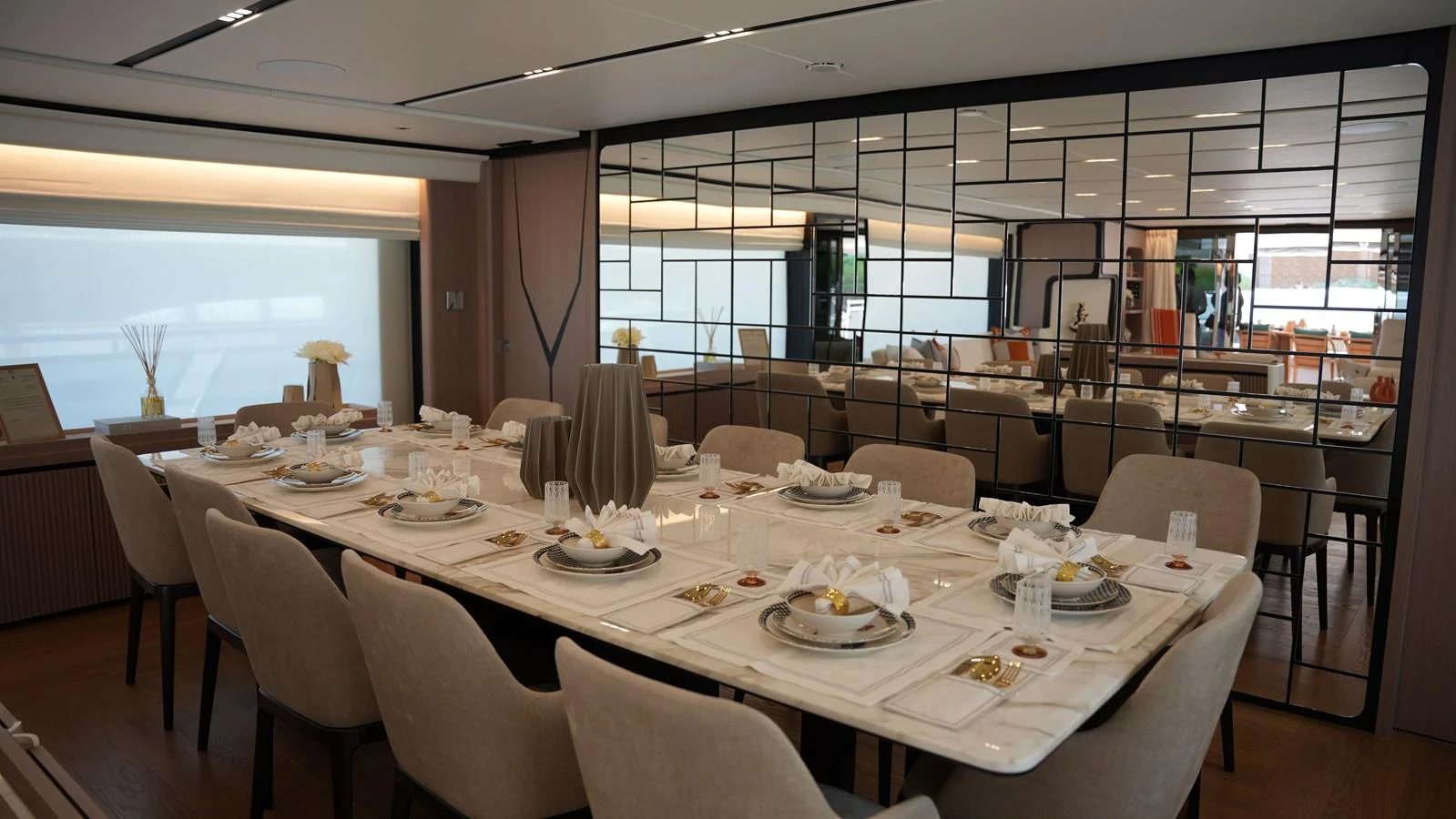 The yacht's dining area features an elegant table setting with plush seating and a mirrored wall enhancing the spacious feel. aboard GEULUNEL Yacht for Sale